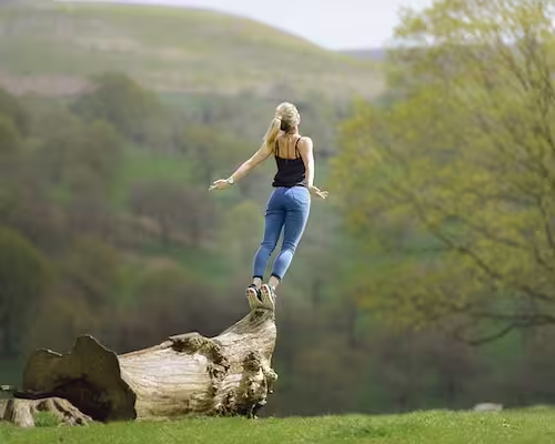femme debout sur un tronc d'arbre prenant son envol les bras tendus en arrière