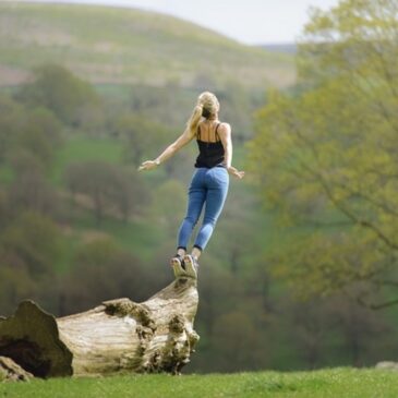 femme dans la nature au bord d'un tronc d'arbre en position saut de l'ange