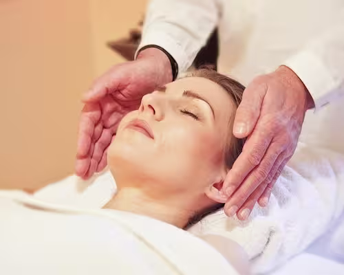 la tête d'une femme allongée recevant un soin reiki avec les mains du praticien autour de sa tête